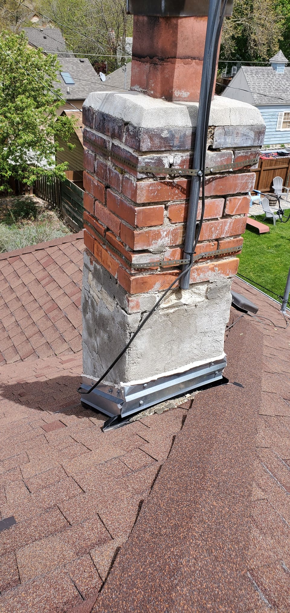 Original brick chimney with metal strapping wrapped around it and a cracked crown above a red shingle roof