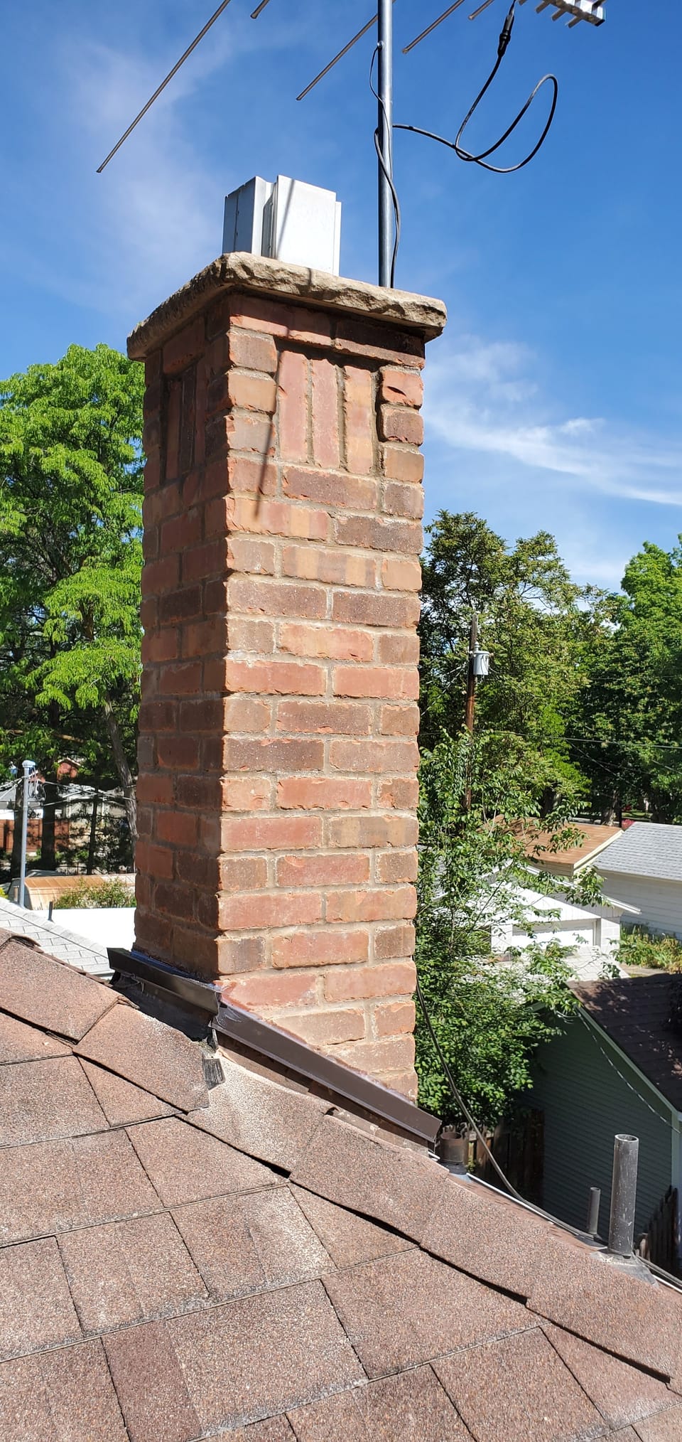 New brick chimney with a recessed panel and stone crown, fresh flashing where it meets the shingle roof