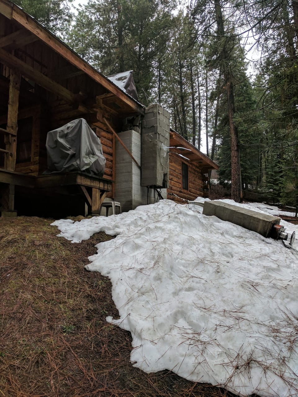 Log cabin with its block chimney broken off at the roofline and the crown lying in snow