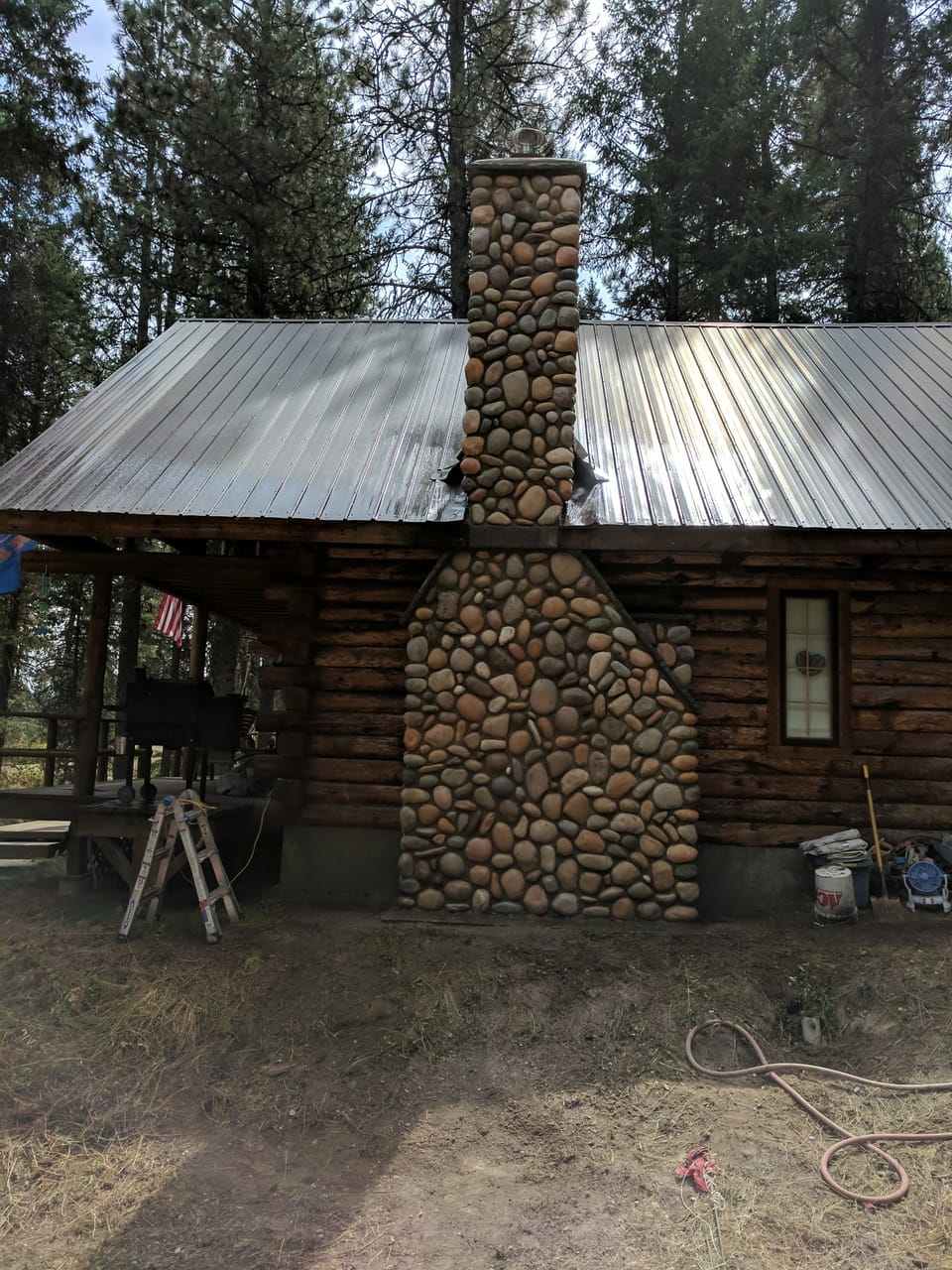 Completed manufactured river rock chimney running from the ground to the crown up the log cabin's metal roof