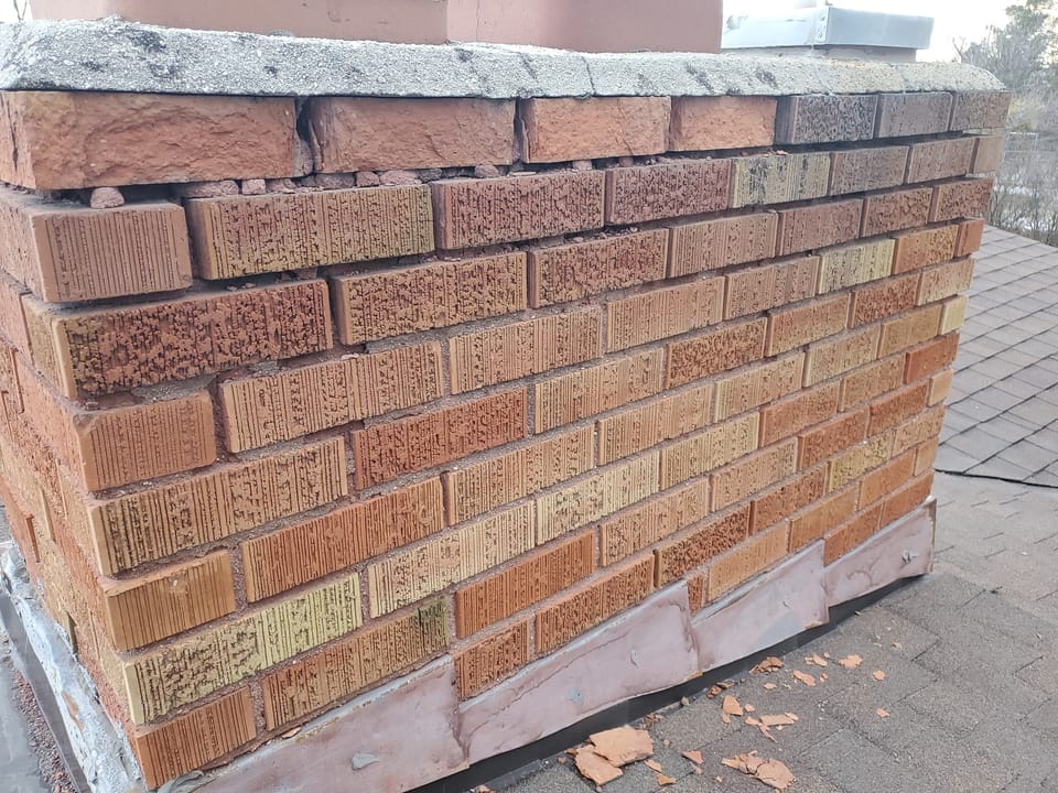 Deteriorated brick chimney before repair with eroded mortar joints, spalled brick and a cracked concrete crown