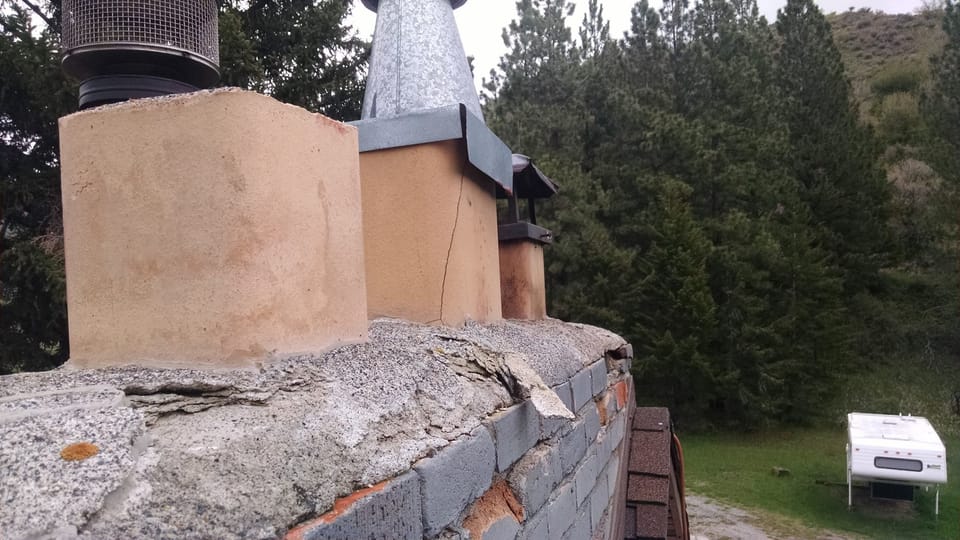 Crumbling concrete crown breaking apart on top of a painted brick chimney above the roof