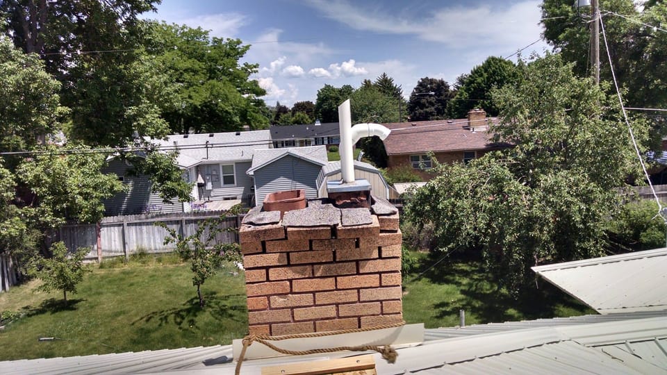 Brick chimney above a metal roof with a broken crown and loose top courses of brick sitting unbonded