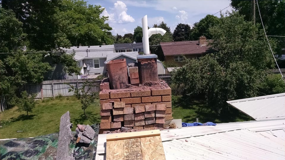 Chimney with crown and loose brick removed, two clay flue liners standing exposed above crumbling mortar
